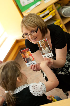 A teacher helps a young girl to
                  identify herself from a picture held at eye level. Taken from the teacher's point
                  of view