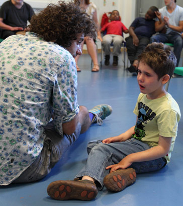 A carer and boy sitting together on the floor of a large room