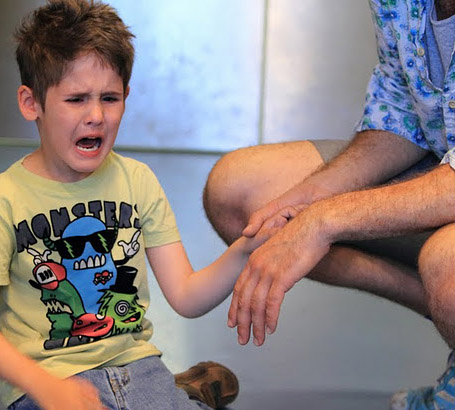 a young boy is consoled and comforted by a male teacher who is halfway out of
                  the frame