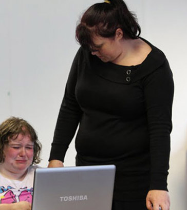 Two teachers comfort a distressed pupil
                  who is using a laptop
