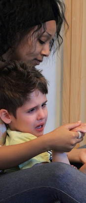 A female teacher comforts a distressed young boy on her lap