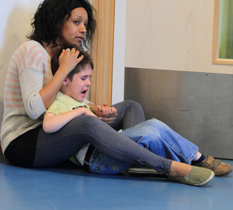 A young female teacher comforts an anxious young boy
