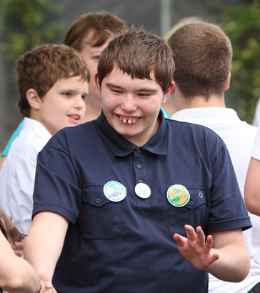 a teenage boy shakes hands with his teacher
                  in a playground full of his peers