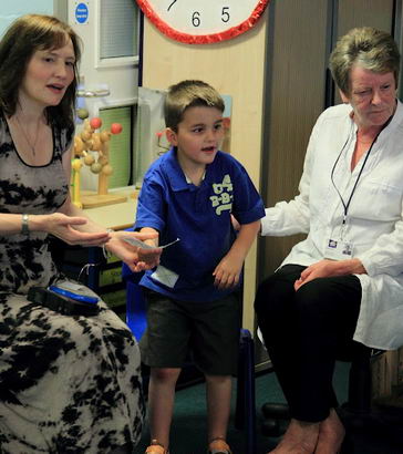 A boy stands between two seated teachers.