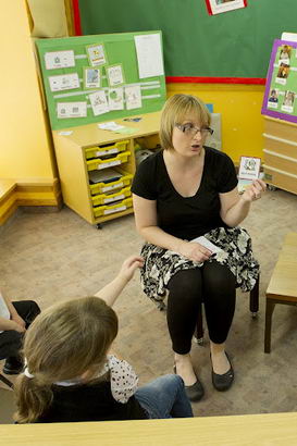 A teacher holds up a card in front
                  of several seated children