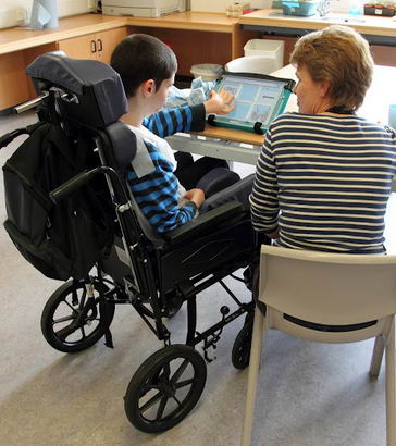 A speech therapist working with a boy
                  using a communcation device