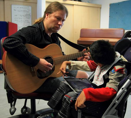 A boy listens to a man playing a guitar