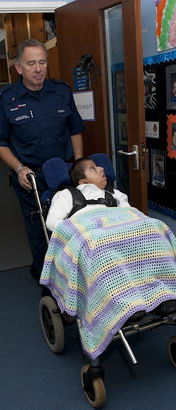 : A boy in a wheelchair, covered
                  in a blanket, is wheeled along a school corridor