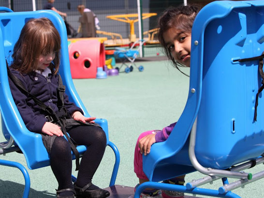 Two girls sit in a seat in a playground