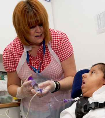 A carer helps to feed a boy via
                  a feeding tube