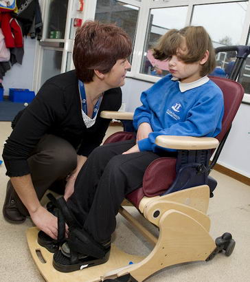 A carer helps to secure a girl
                  in a specialist chair