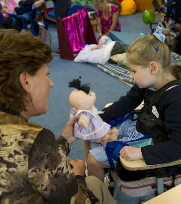 A teacher holds a doll in front
                  of a girl in a specialist chair