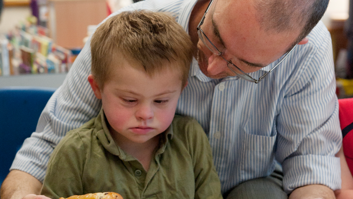 A teacher sits behind a boy
                  helping him with his food selection