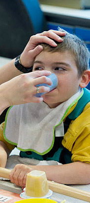 A carer helps a boy to drink from
                  a cup