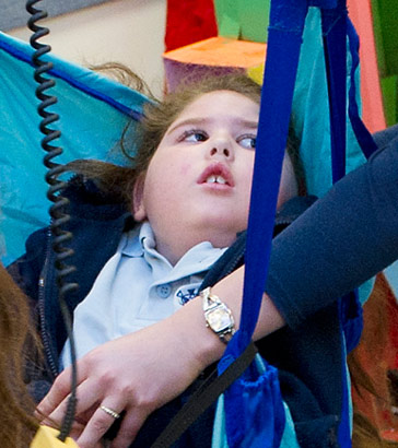 Two carers use specialised equipment
                  to lift a child into a wheelchair