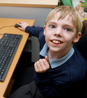 A boy sitting in front of a computer
                  smiling at the camera