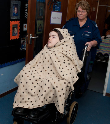 A child wearing a cover being pushed
                  in a wheelchair