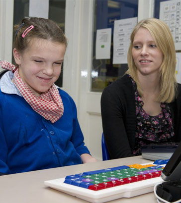 A boy in a specialist chair with his teacher
                  smiling