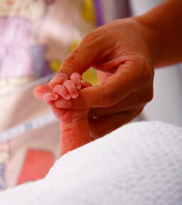 Newborn holding mother's
                  finger.