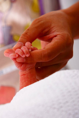 Newborn holding mother's
                  finger.