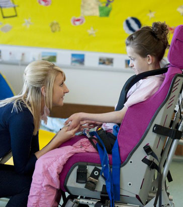 Teacher helping a disabled girl play with
                  a spinning top