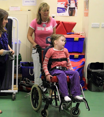 Girl in a wheelchair being pushed by
                  a teacher