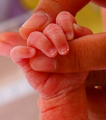 Newborn holding mother's
                  finger.