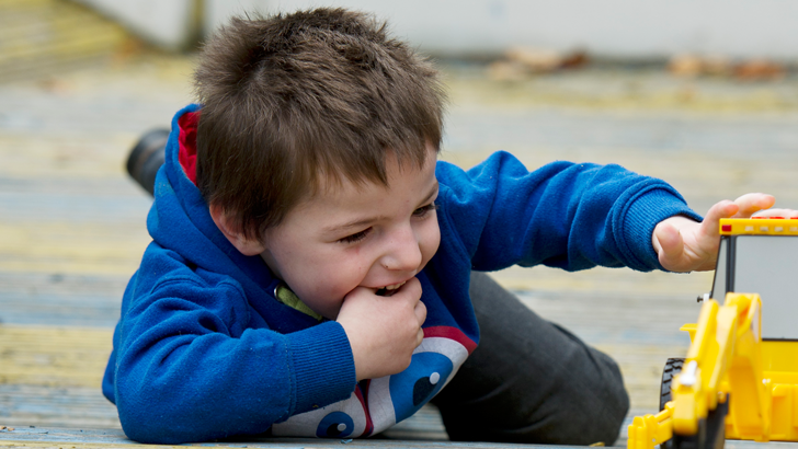 A smiling boy lies on the ground
                  playing with a toy digger
