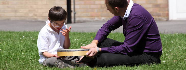 A teacher and a boy sit on the grass with
                  a large drum