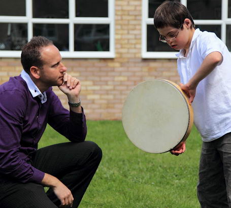 A teacher watches a boy play with a large
                  drum