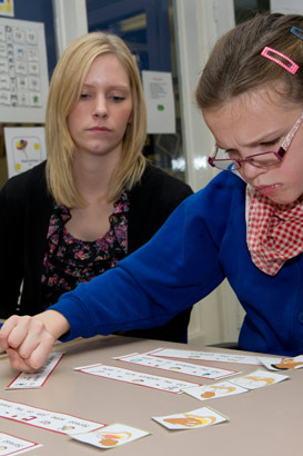 A teaching assistant watches a girl
                  rearrange some paper sentences on a table