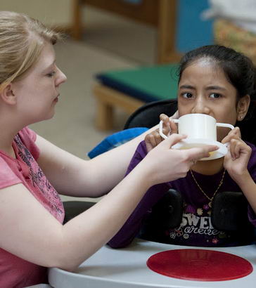 A carer helps a girl drink from a cup