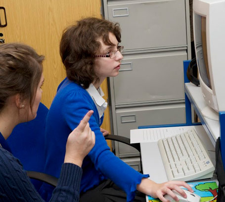 A teacher watches a girl using a computer
