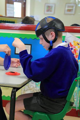 A teacher sits opposite a boy and shows him different objects