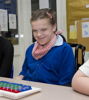 A girl and her teacher sit in front of a keyboard smiling