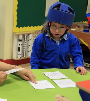 A girl wearing head protection looks at some cards laid out by a teacher