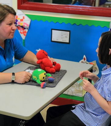 A teacher offers a girl a choice of two toys