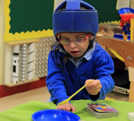 girl wearing head protection chooses a spoon from a set of objects on a table