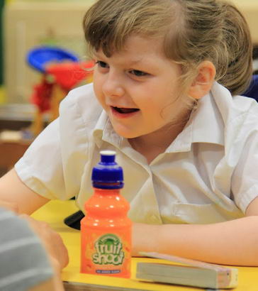 A girl sitting opposite her teacher smiles during an assessment