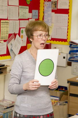 A teacher holds up a self-assessment card depicting a green disc
