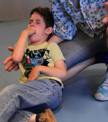 A distressed boy with his hand in his mouth is comforted by a teacher