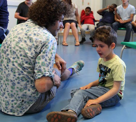 A boy and a teacher sit outside a circle of children and adults