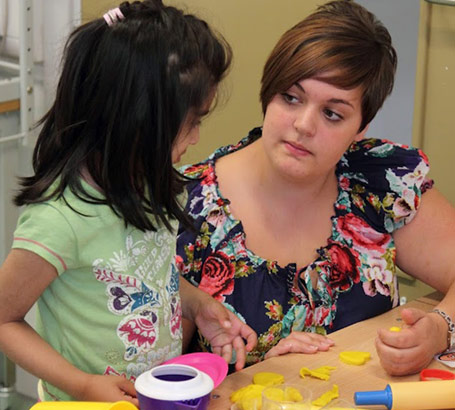 A girl and a teacher beside a table covered in various brightly coloured objects
