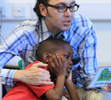 A boy raises his hands to his face as a teacher reads from a card